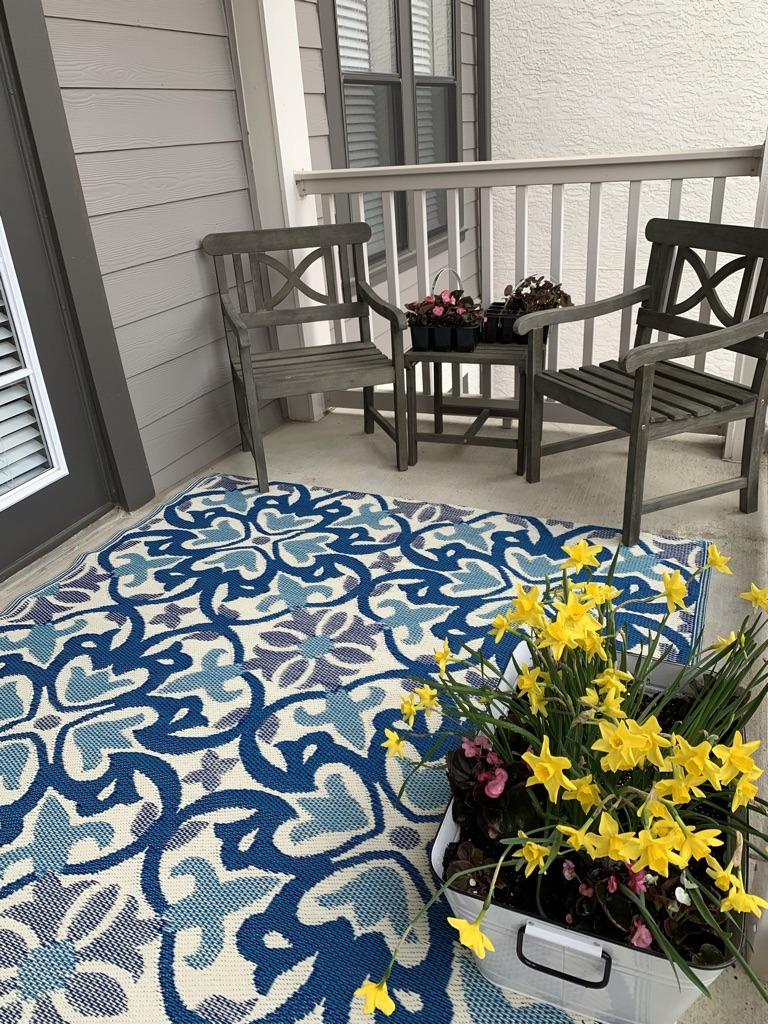View of seating, outdoor rug, and flowers on an apartment balcony