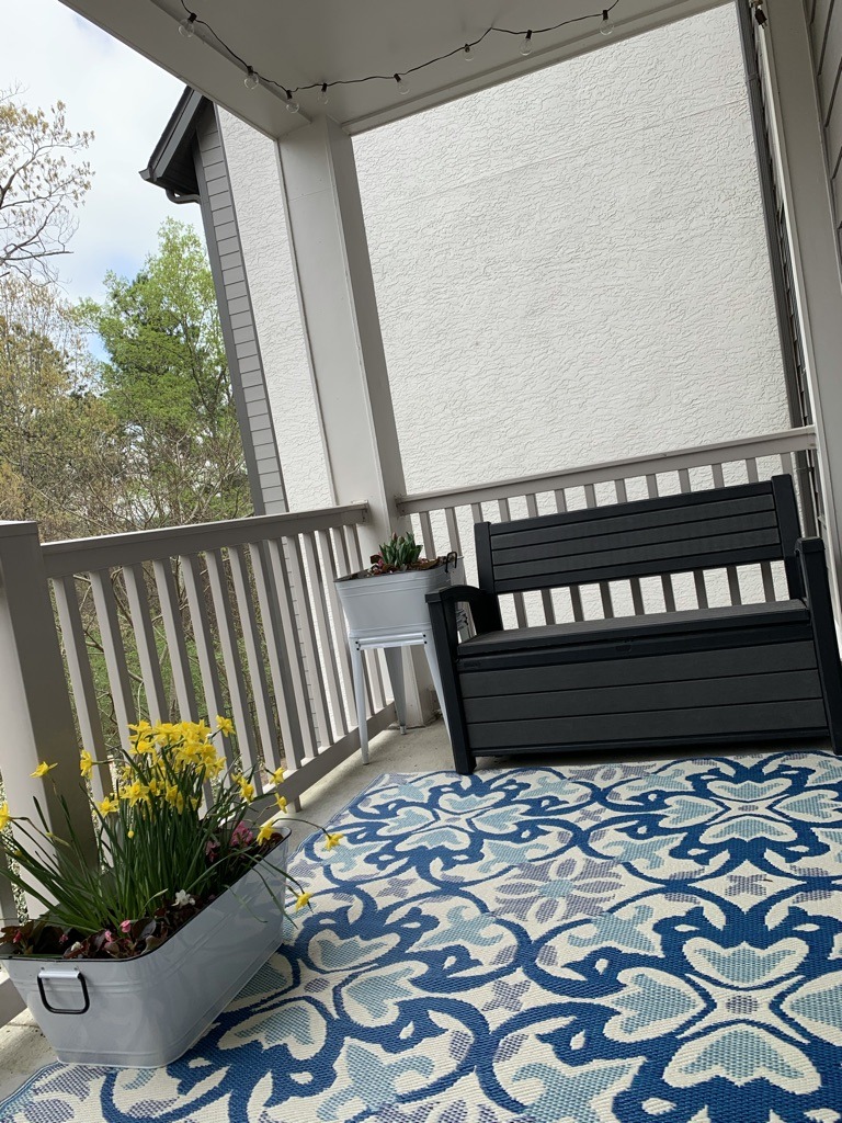 View of apartment balcony with seating, outdoor rug, and flowers